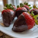 A close-up of several glossy chocolate covered strawberries arranged on a white plate.
