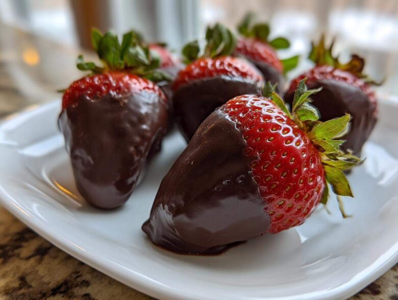 A close-up of several glossy chocolate covered strawberries arranged on a white plate.