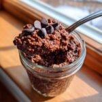 A spoonful of rich chocolate overnight oats topped with chocolate chips being lifted from a glass jar.