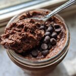 Overhead view of rich chocolate overnight oats in a jar, topped with chocolate chips and a spoonful being lifted out.