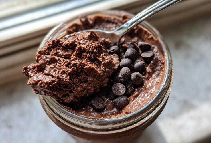 Overhead view of rich chocolate overnight oats in a jar, topped with chocolate chips and a spoonful being lifted out.