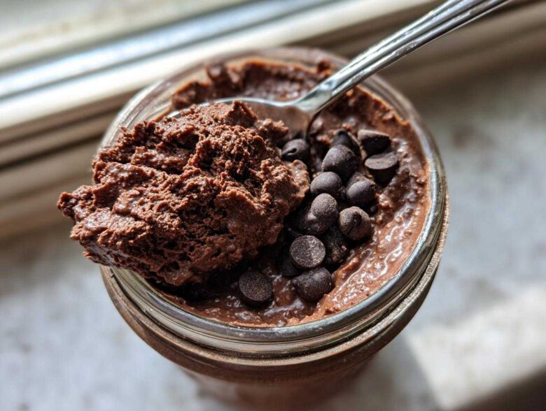 Overhead view of rich chocolate overnight oats in a jar, topped with chocolate chips and a spoonful being lifted out.