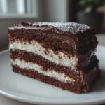 A rich slice of chocolate yule log cake featuring dark sponge layers and thick white cream filling, topped with ganache.