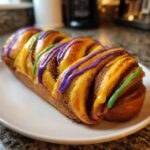 A close-up of a freshly baked, braided king cake loaf drizzled with purple, yellow, and green icing.