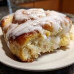 A close-up of a single, fluffy serving from a cinnamon roll casserole, generously topped with white icing.