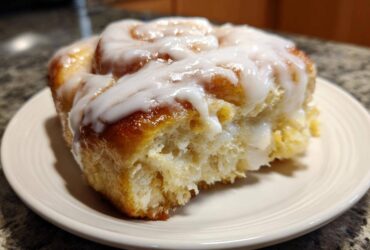 A close-up of a single, fluffy serving from a cinnamon roll casserole, generously topped with white icing.