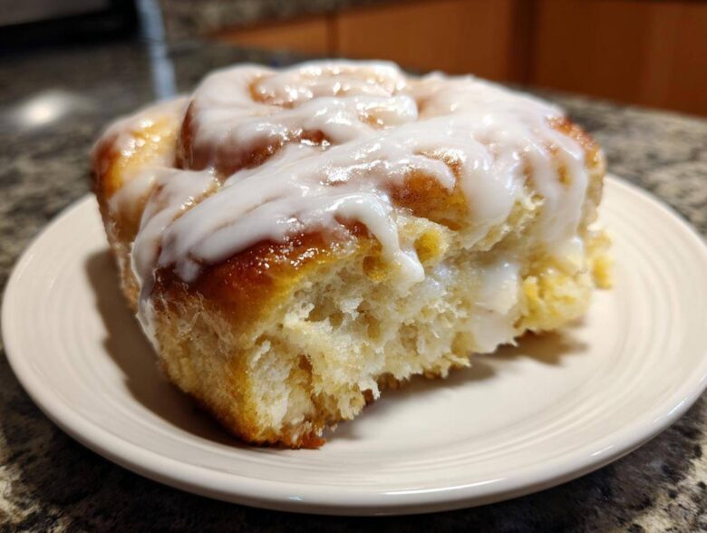 A close-up of a single, fluffy serving from a cinnamon roll casserole, generously topped with white icing.