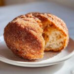 A close-up of a freshly made Mexican buñuelos dusted heavily with cinnamon sugar, showing the fluffy interior.