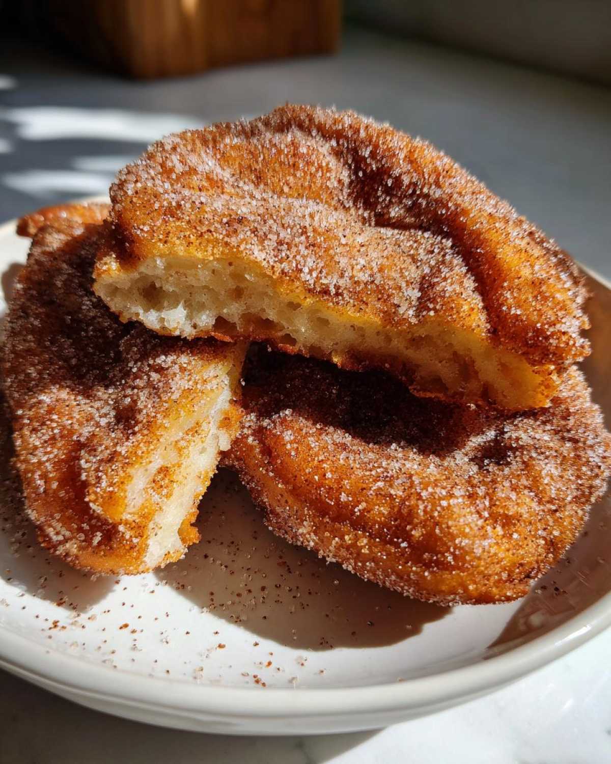 Two golden brown Mexican buñuelos coated heavily in cinnamon sugar, one cut open to show the fluffy interior.