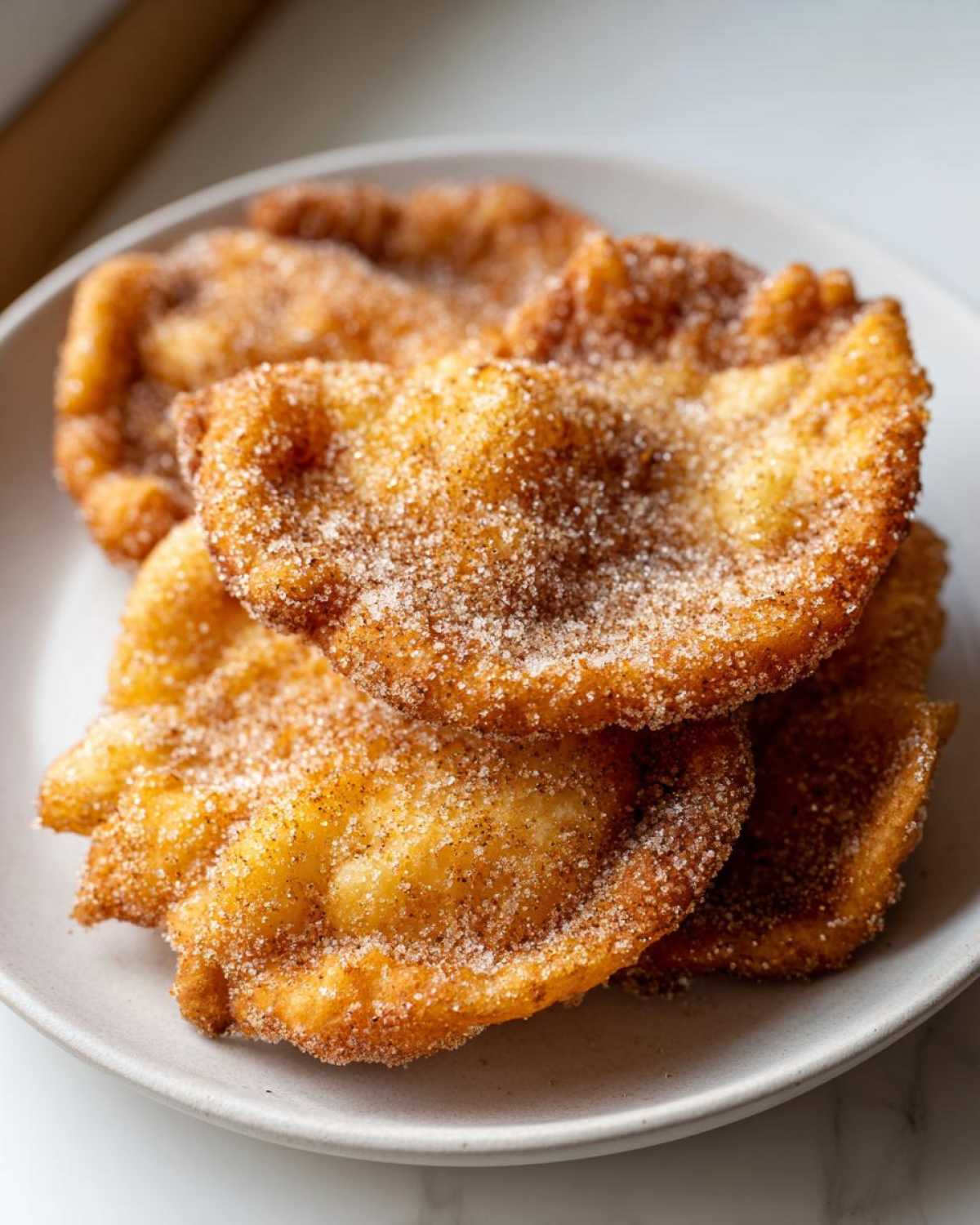 A stack of golden-brown, freshly fried Mexican buñuelos generously coated in cinnamon sugar.