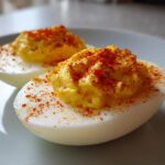Two halves of classic deviled eggs topped with creamy yolk filling and sprinkled with bright red paprika.