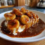 Close-up of caramelized bananas in rich sauce, part of a delicious bananas foster dessert served over cream.