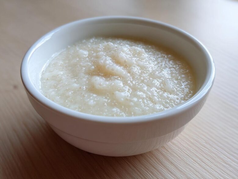 A close-up of creamy, pale coconut chia pudding served in a small white bowl on a light wooden surface.
