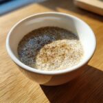 A close-up of creamy coconut chia pudding topped with spices in a white bowl on a wooden table.
