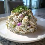 A mound of creamy cottage cheese chicken salad mixed with celery and red onion, topped with fresh dill.