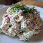 A mound of creamy cottage cheese chicken salad mixed with red onion and topped with fresh dill.