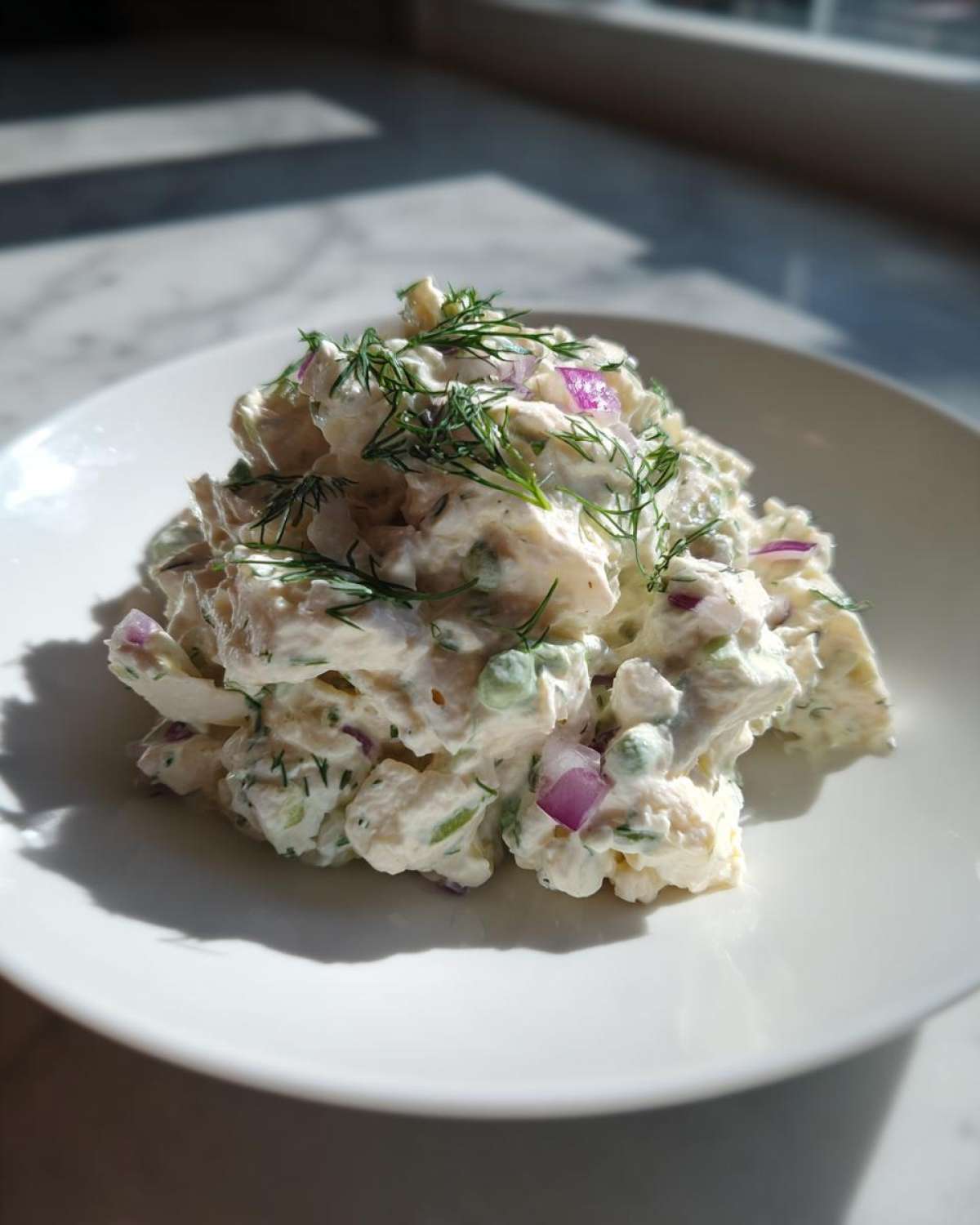 A scoop of creamy cottage cheese chicken salad mixed with red onion and peas, topped with fresh dill.