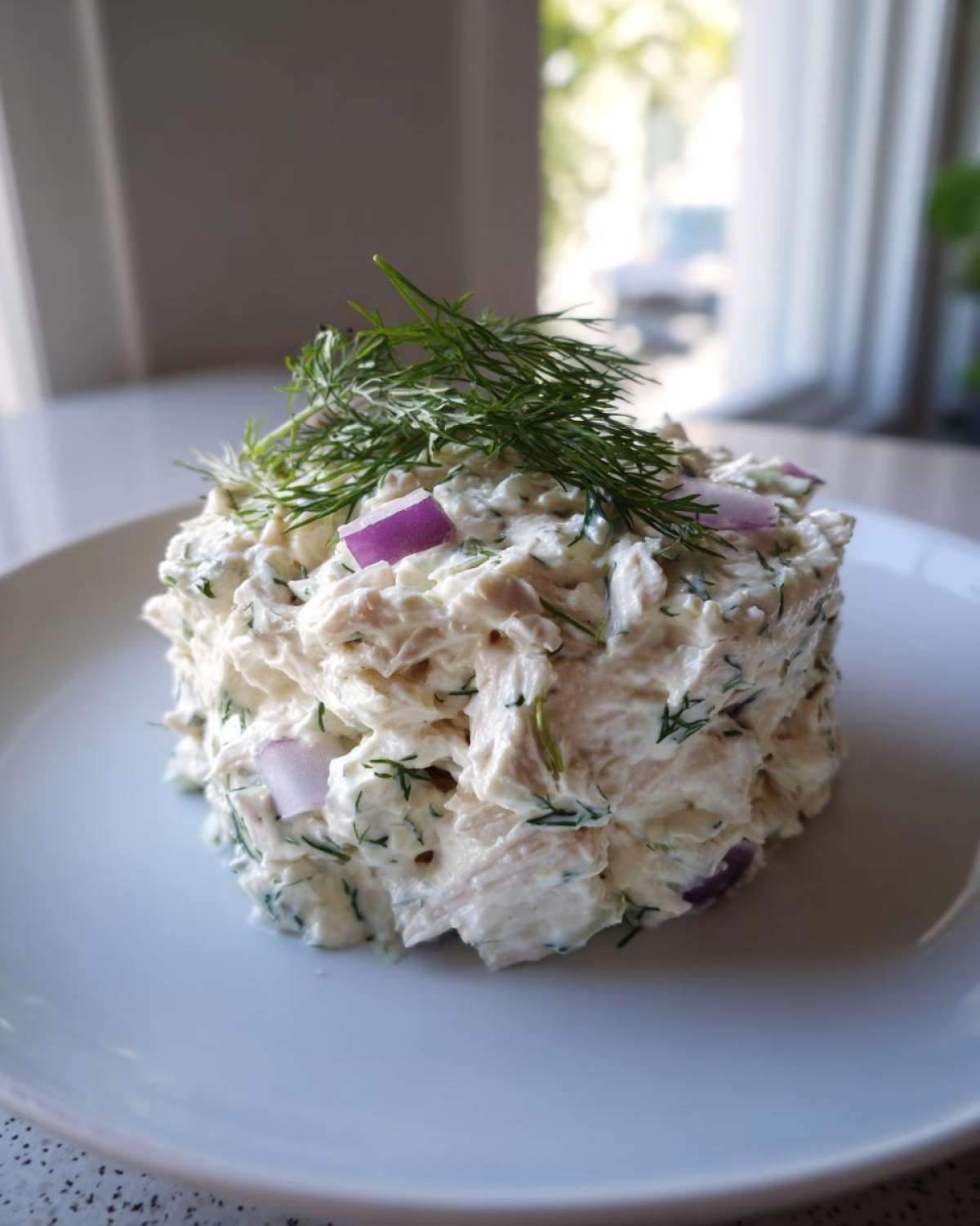 A mound of creamy cottage cheese chicken salad garnished with fresh dill and red onion on a white plate.