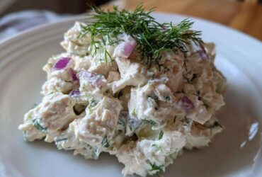 A mound of creamy cottage cheese chicken salad mixed with red onion and topped with fresh dill.