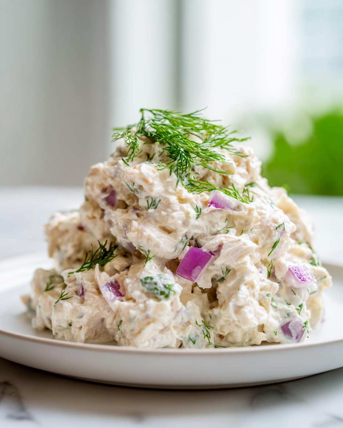 A mound of creamy cottage cheese chicken salad mixed with red onion and topped with fresh dill.
