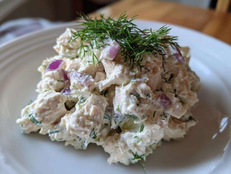 A mound of creamy cottage cheese chicken salad mixed with red onion and topped with fresh dill.