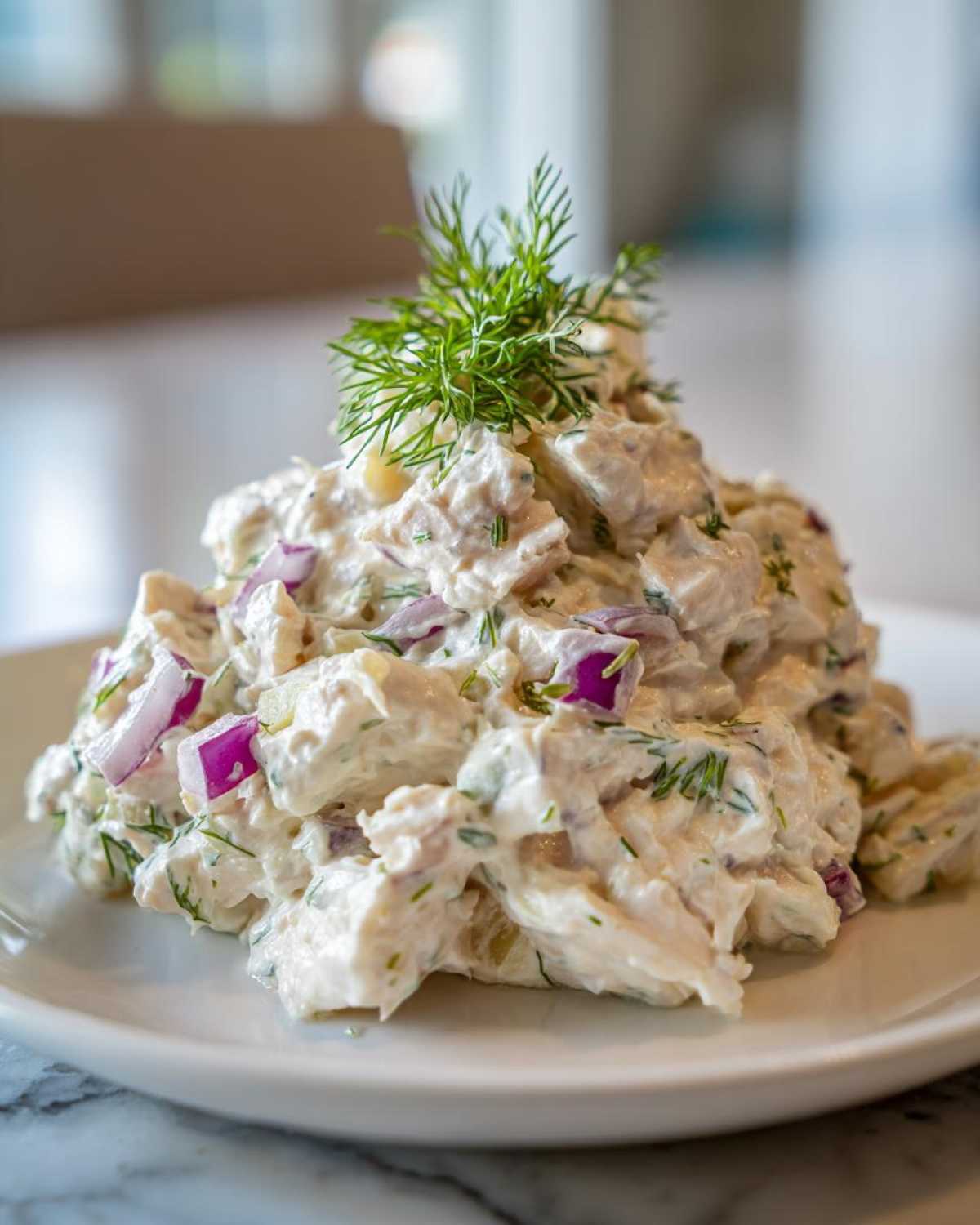 A mound of creamy cottage cheese chicken salad mixed with red onion and topped with fresh dill.