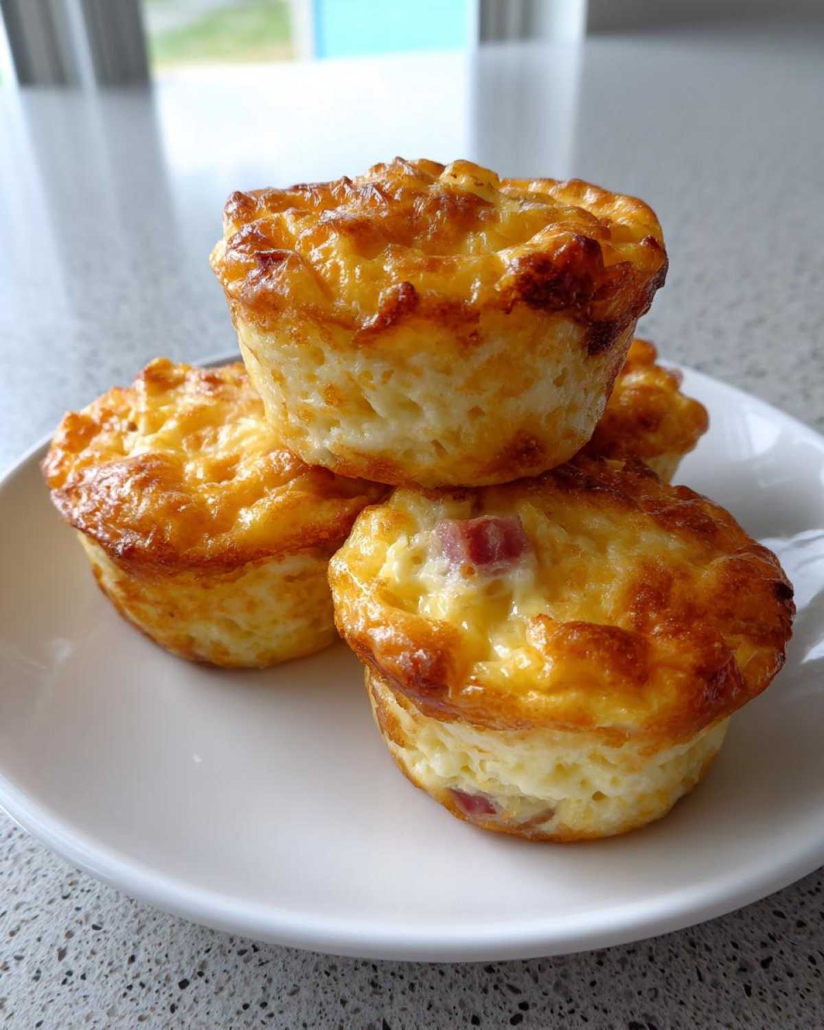 Three golden brown cottage cheese egg cups stacked on a white plate, showing a cheesy, baked top.