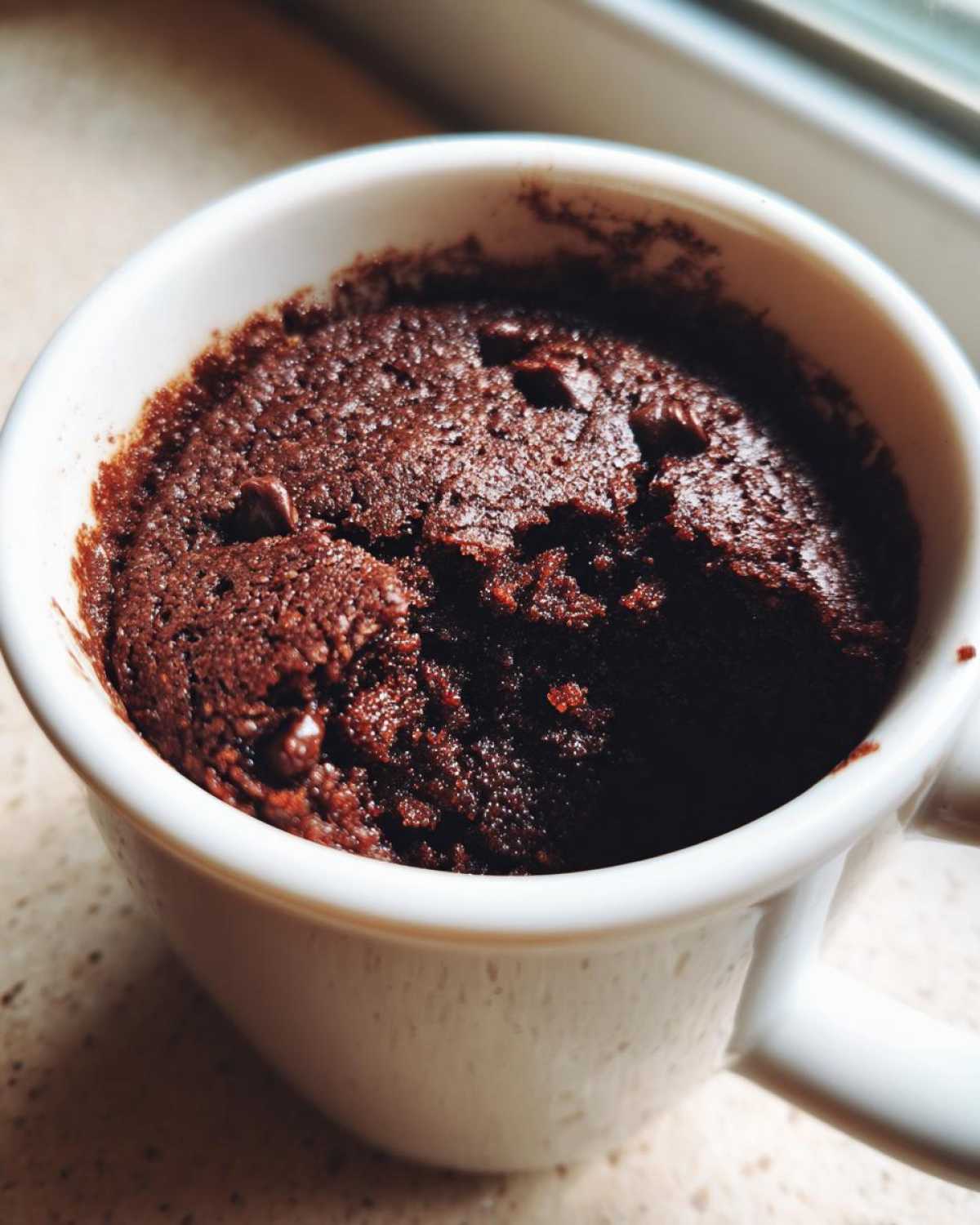 Close-up of a rich, dark chocolate Cottage Cheese Microwave Brownie baked inside a white mug.