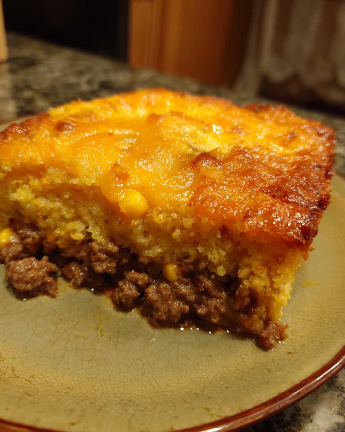 Close-up of a slice of cowboy cornbread casserole showing a savory ground meat layer beneath a golden, cheesy cornbread topping.