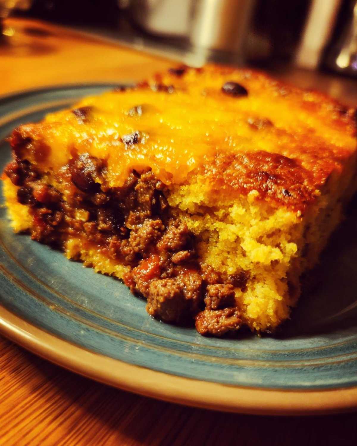 Close-up of a slice of cowboy cornbread casserole featuring a layer of seasoned ground beef and topped with melted cheddar cheese.