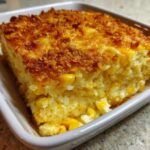 A close-up of a square serving of moist cream cheese corn casserole with a crunchy, browned topping.