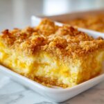 A close-up of a square slice of rich cream cheese corn casserole with a golden, crunchy topping.