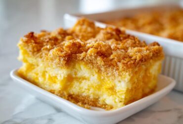 A close-up of a square slice of rich cream cheese corn casserole with a golden, crunchy topping.