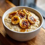 Close-up of creamy banana oatmeal topped with caramelized banana slices and syrup.