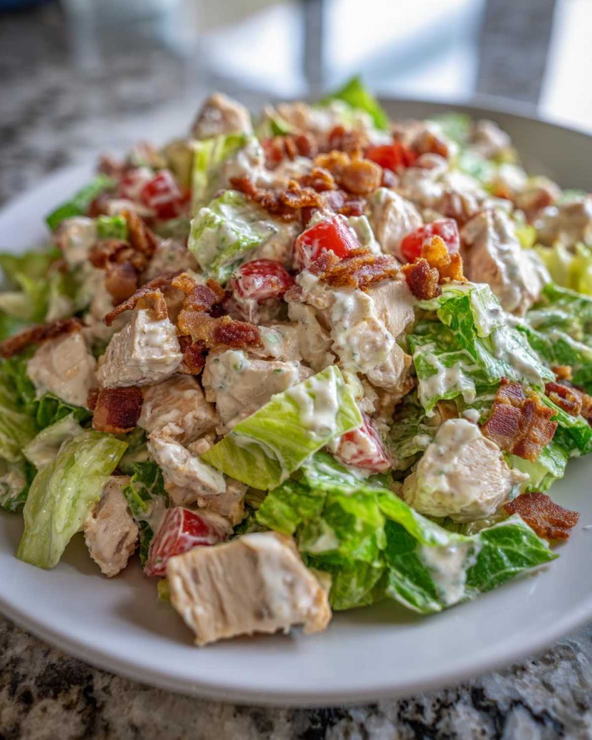 Close-up of a creamy blt chicken salad featuring chunks of chicken, lettuce, tomatoes, and bacon bits.