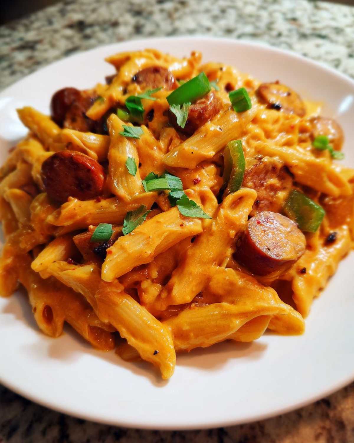 A close-up of creamy cajun sausage pasta featuring penne, sliced sausage, and green onions on a white plate.