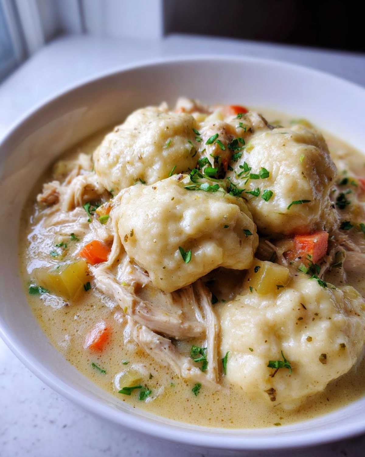 Close-up of a bowl of creamy chicken and dumplings, featuring fluffy dumplings and shredded chicken.