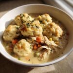 A close-up of a bowl of creamy chicken and dumplings, topped with fluffy dumplings and fresh parsley.