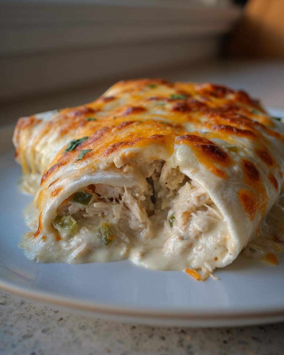 Close-up of creamy white sauce chicken enchiladas, showing shredded chicken filling and melted, browned cheese topping.
