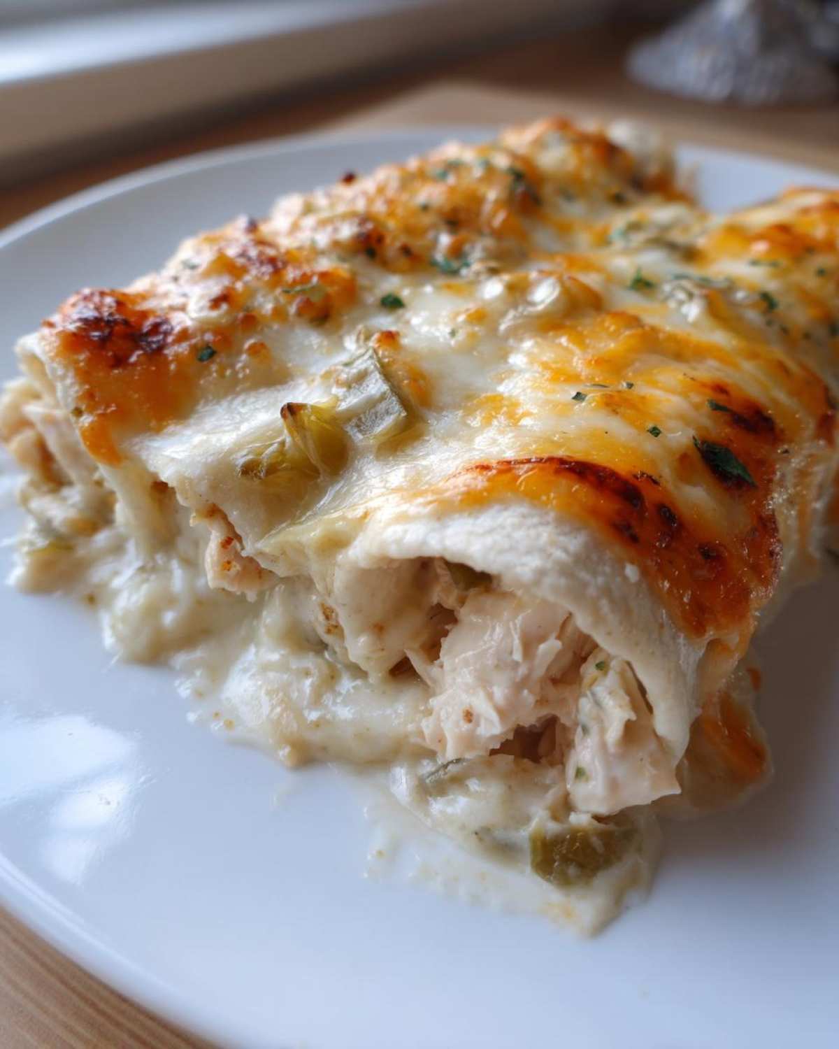 Close-up of creamy white sauce chicken enchiladas topped with melted, browned cheese and parsley.