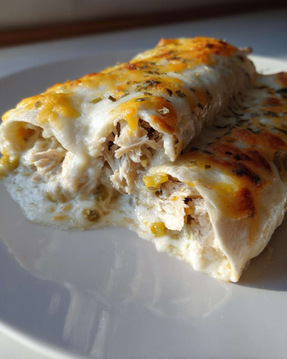 Close-up of creamy white chicken enchiladas cut open to show shredded chicken filling and melted cheese sauce.
