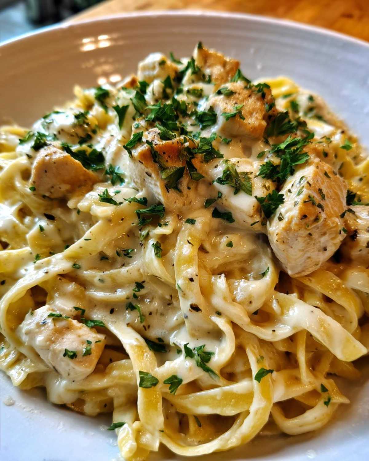 Close-up of creamy chicken fettuccine alfredo pasta topped with diced chicken and fresh parsley.