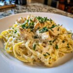 Close-up of creamy chicken fettuccine alfredo pasta topped with grilled chicken pieces, Parmesan, and fresh parsley.