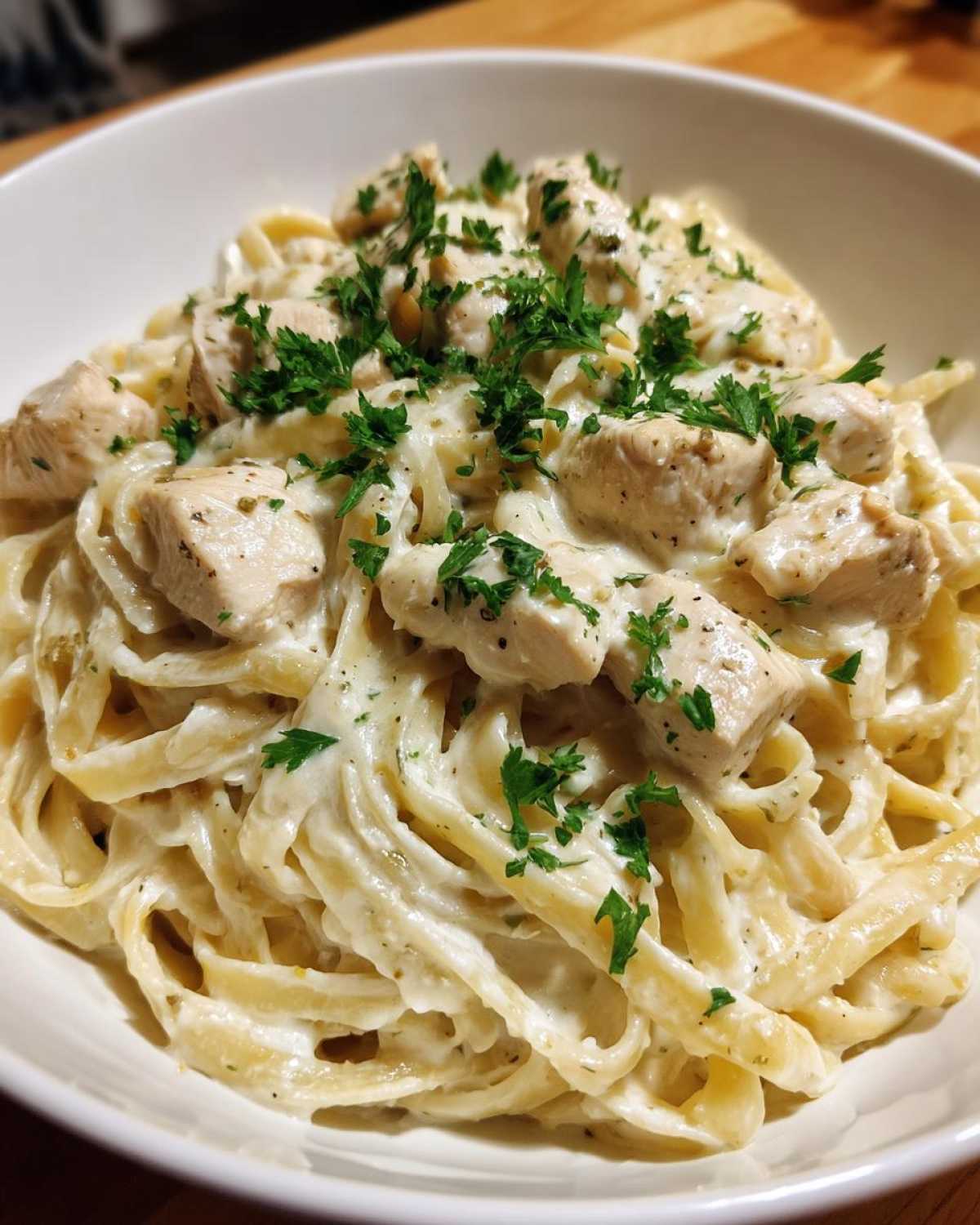 Close-up of creamy chicken fettuccine alfredo pasta topped with diced chicken and fresh parsley.