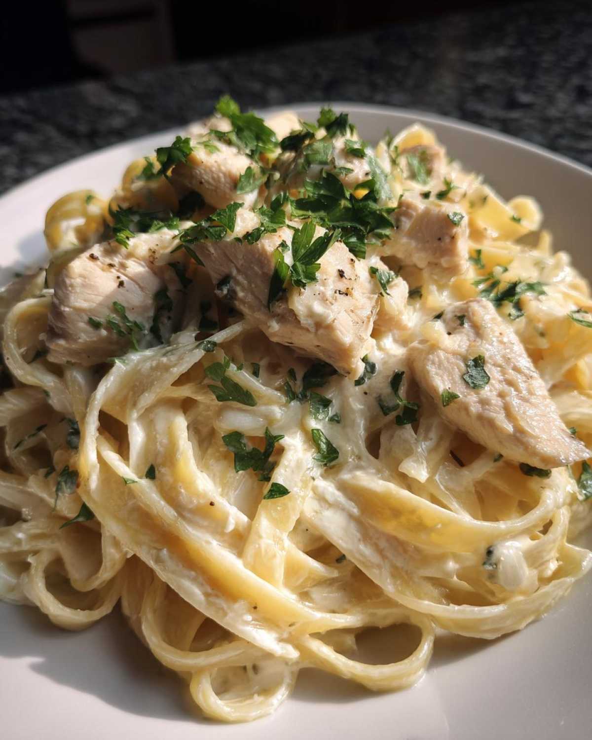 Close-up of creamy chicken fettuccine alfredo topped with chopped parsley and black pepper.