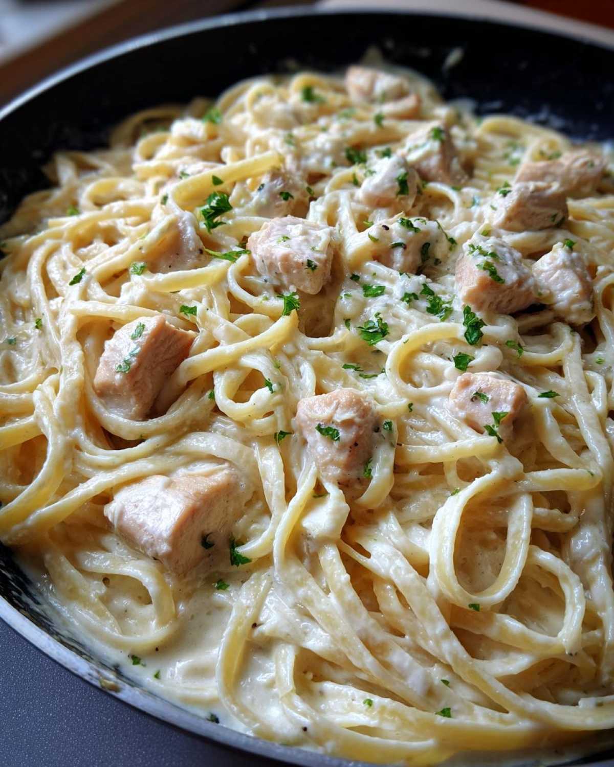 Close-up of creamy chicken fettuccine alfredo tossed in a black skillet and garnished with parsley.
