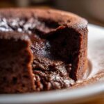 Close-up of a rich, dark chocolate pudding dessert with a molten, creamy center oozing out.