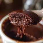 A spoonful of rich, creamy chocolate pudding being lifted from a small white ramekin.
