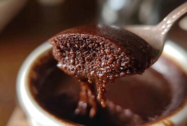 A spoonful of rich, creamy chocolate pudding being lifted from a small white ramekin.