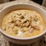 Close-up of a bowl filled with creamy crockpot white chicken chili, topped with shredded chicken and green chilies.